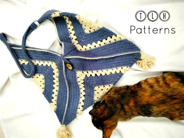 A blue crochet bag with wooden toggle closure on a n=bed with a cat.