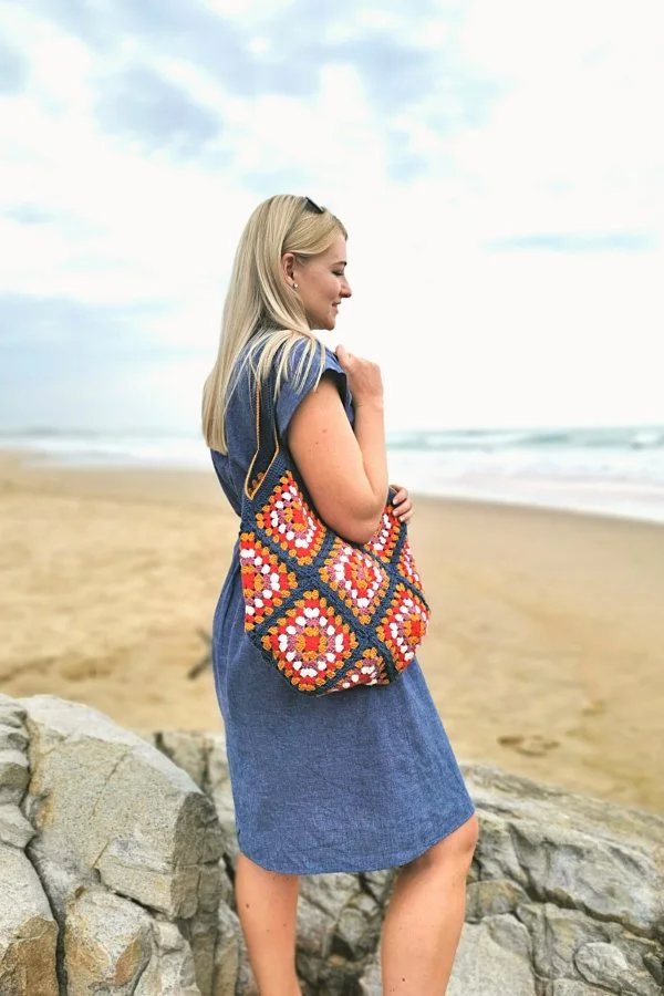A woman at the beach carrying a brightly coloured crochet bg.