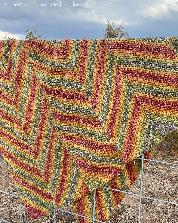 A chevron striped c2c crochet blanket hanging over a fence.