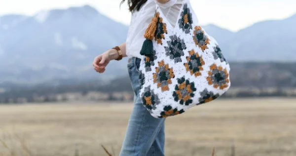 A large granny square tote bag slung over a womans shoulder.