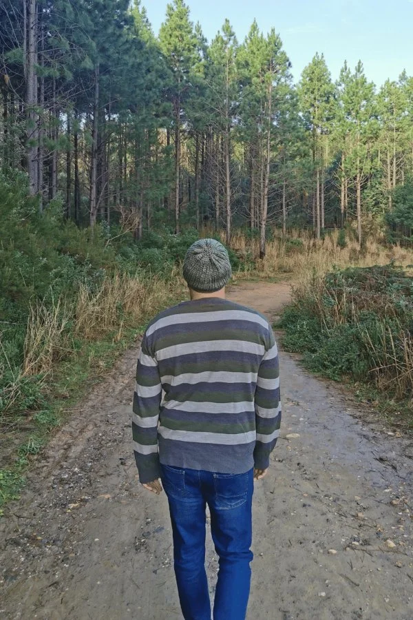 A man walking in the woods wearing a crochet beanie.