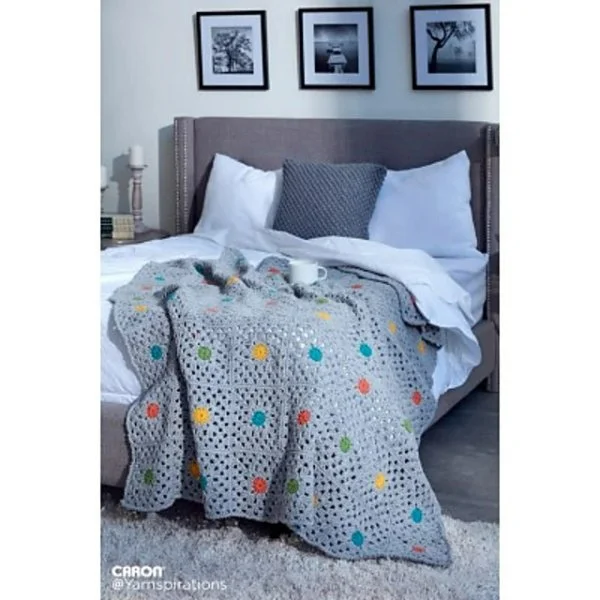 A bed with a crochet blnaket draped over the bottom corner.
