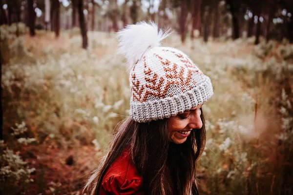 A  woman wearing a crochet colourwork hat with a pine tree motif.