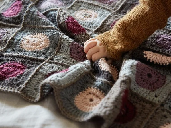 A babies hand pulling on a crochet baby blanket.