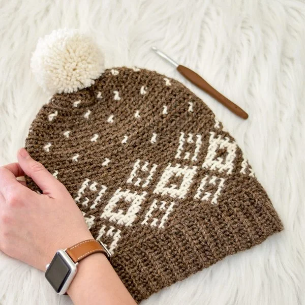A brown and white fair isle crochet beanie with white pompom.