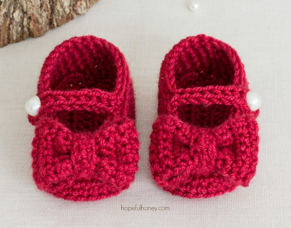 Red crocheted baby Mary Jane shoes with bows and pearl buttons.