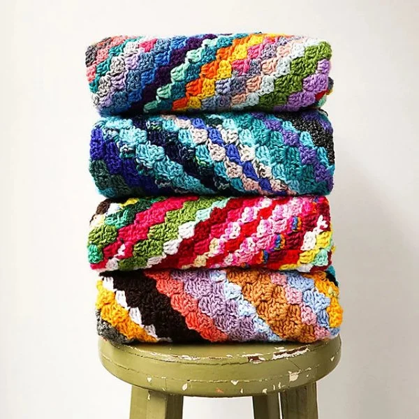 A stack of colourful C2C crochet blankets on an old green stool.