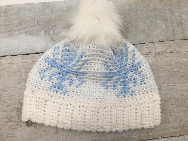 Blue and white tapestry crochet beanie on a wooden board.