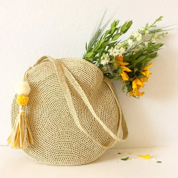 A crochet circle bag with tassel and yellow flowers.
