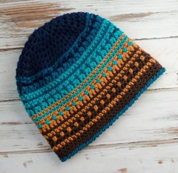 A multicoloured men's crochet hat on a white board background.