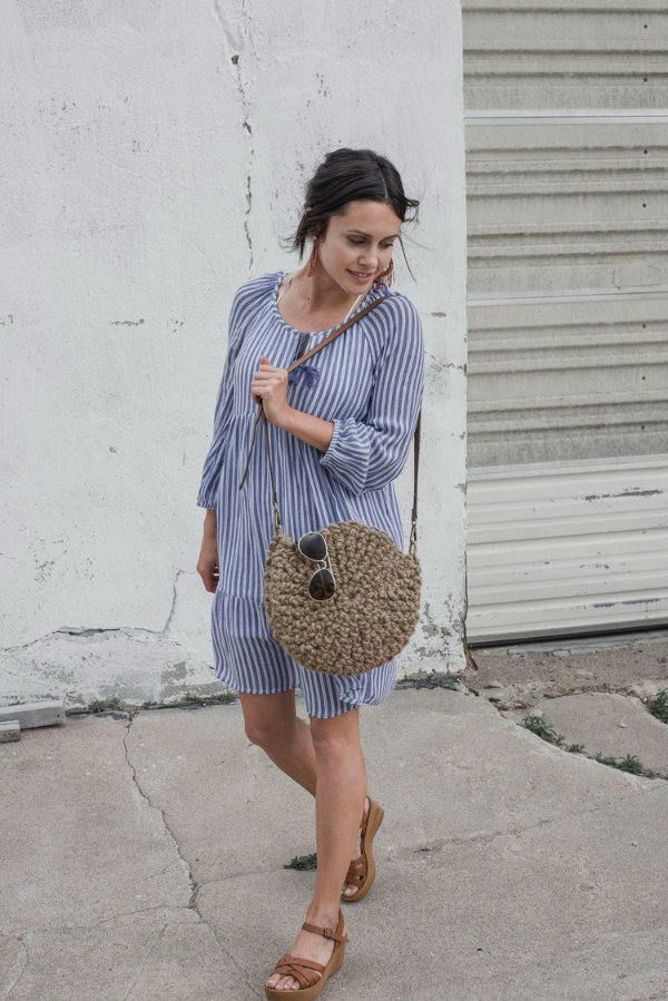 A woman holding a crochet jute bag and sunglasses.