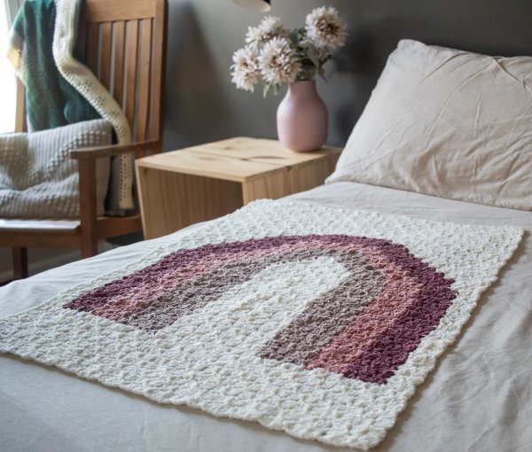 A rainbow c2c crochet baby blanket on a bed.