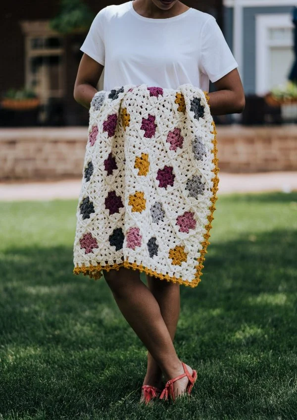 A woman holding a granny square baby blanket in her arms.