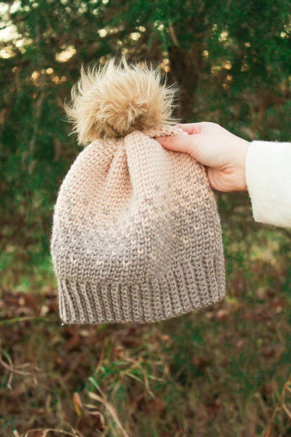 Someone holding a Fair Isle crochet beanie with a faux fur pompom.