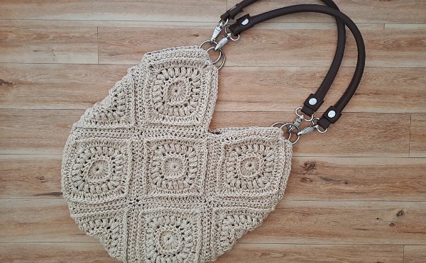 A granny square bag with leather handles on wooden background.