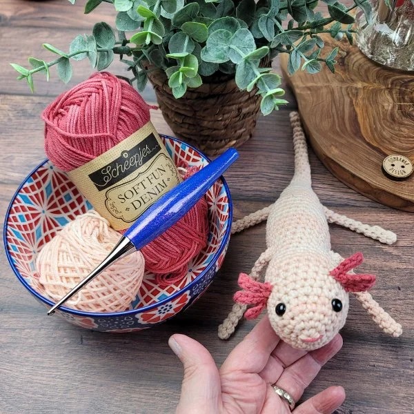 A realistic-looking crochet axolotl with a bowl of crochet supplies.