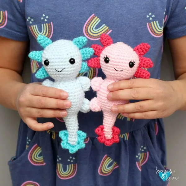 A child holding two crochet axolotl toys.