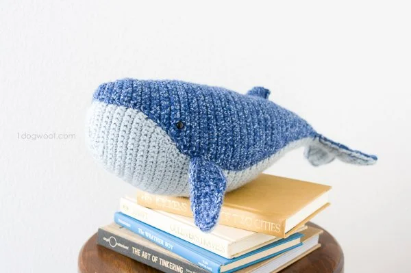 A crochet baby humpback whale plushie resting on a stack of books.