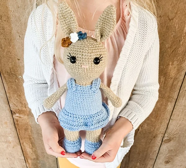 Crochet bunny toy dressed as a girl with a blue dress and flowers.