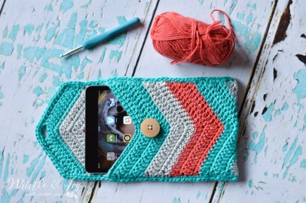 A crochet tablet sleeve with bright chevron stripes on a table with crochet materials.