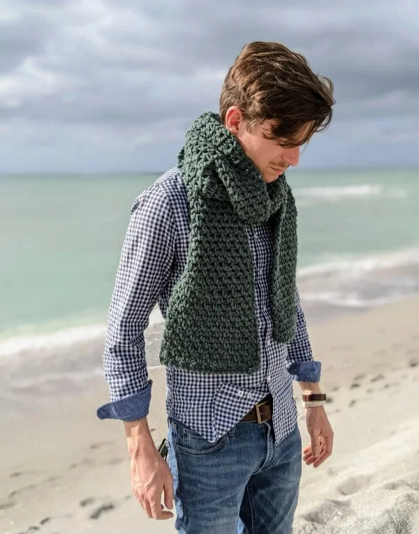 A man wearing a crochet scarf at the beach.