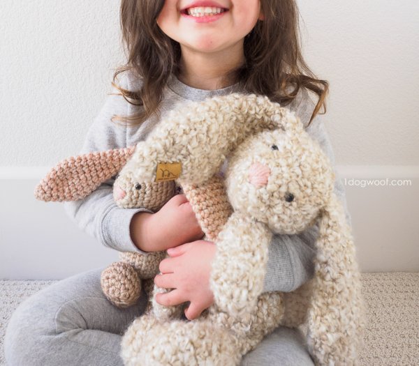 A child cuddling two crochet rabbit softies.