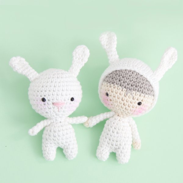 A white crochet rabbit holding hands with a crochet boy in a rabbit costume.