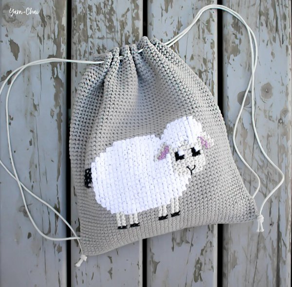 A crochet backpack with a cross-stitch lamb on the front panel.