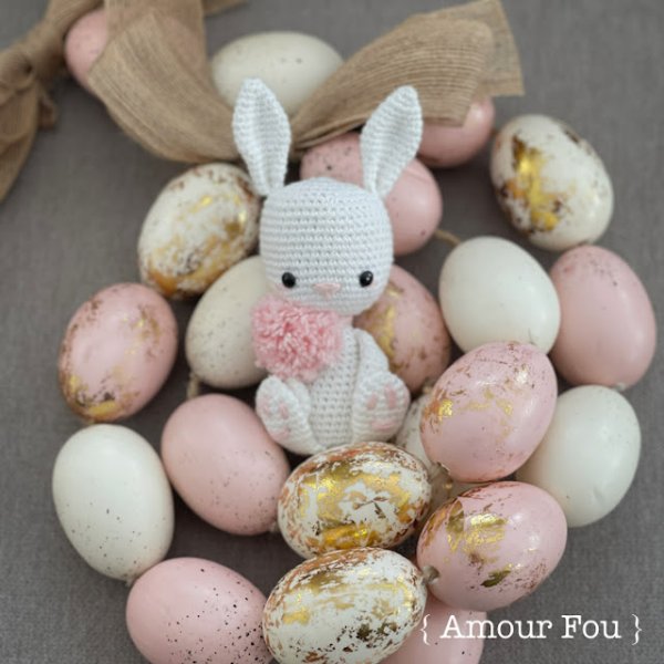 A white crochet rabbit sitting amongst Easter eggs.