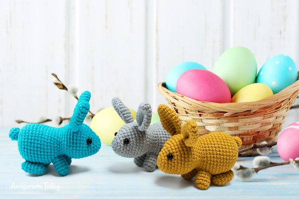 Crochet Easter bunnies next to a basket of coloured eggs.