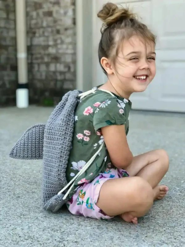 A child wearing a crochet shark backpack.