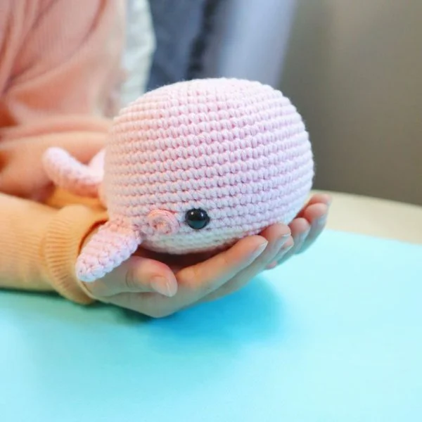A pink crochet whale resting in a hand.