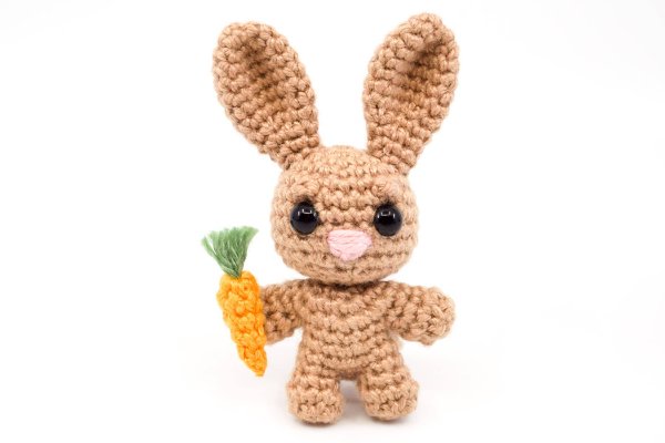 A tiny crochet rabbit holding a carrot.