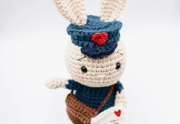 A crochet bunny rabbit in a mailman's costume.