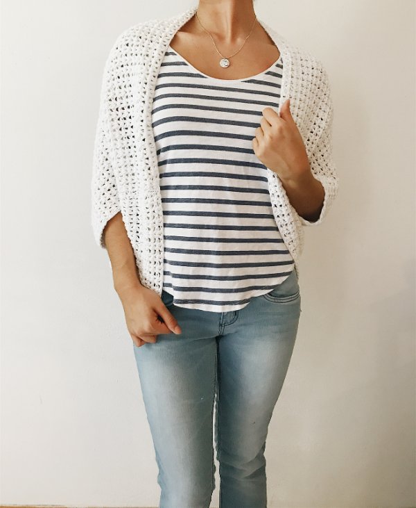 Woman wearing a white crochet shrug with a striped tee and jeans.