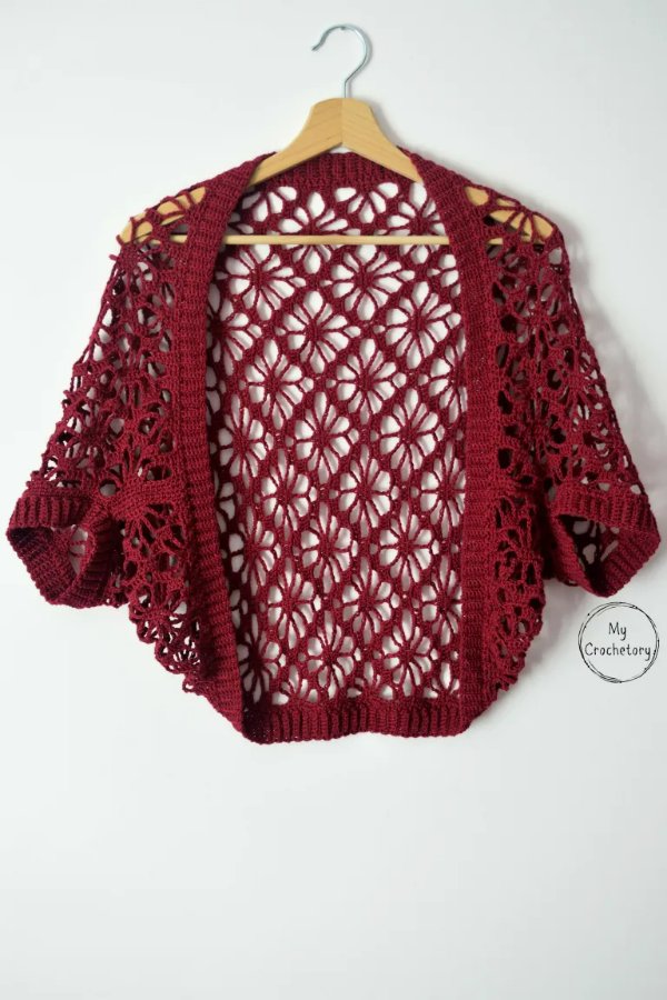 A lacy red crochet shrug on a wooden clothes hanger.
