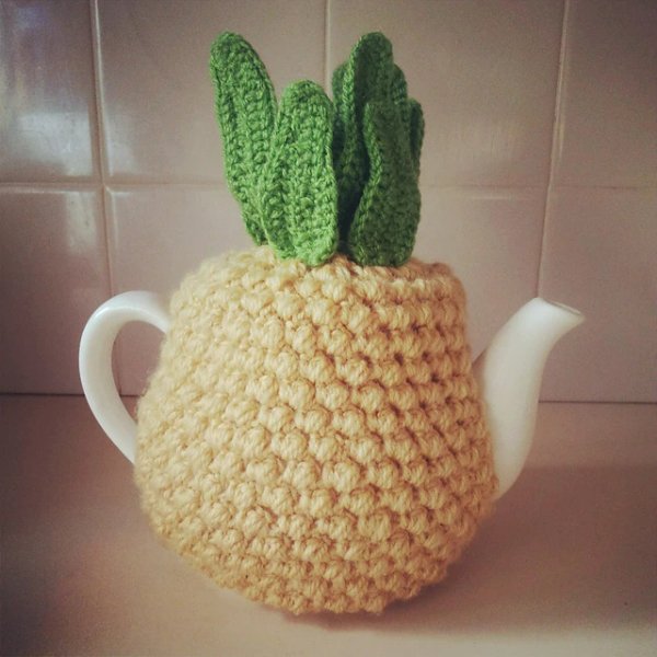 A teapot with a crochet tea cozy that looks like a pineapple.
