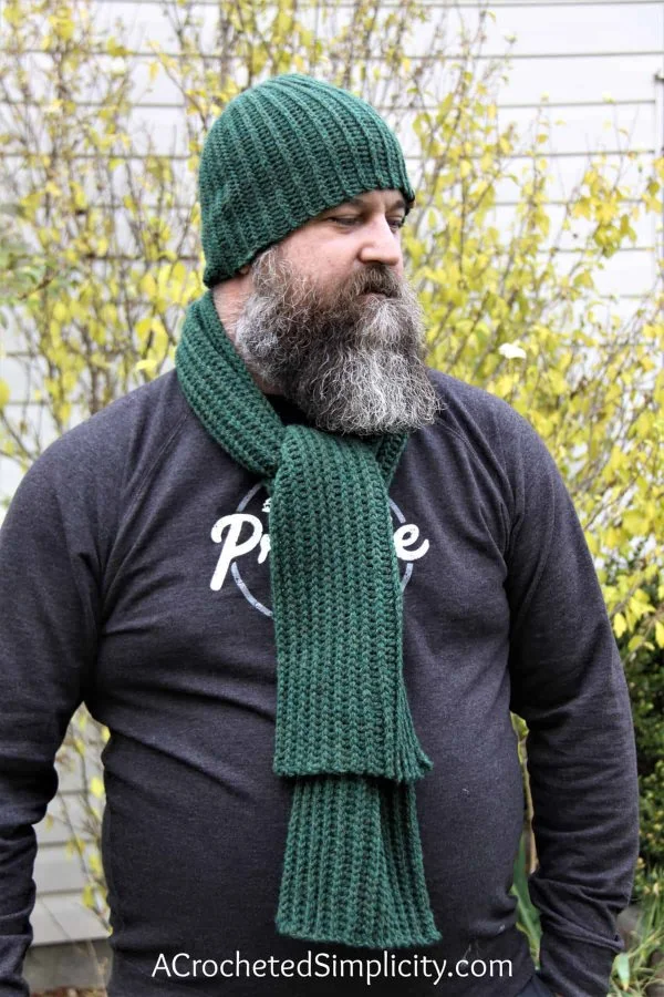 A man wearing a ribbed crochet scarf and matching green beanie.