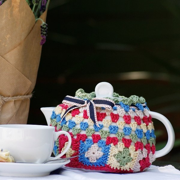 A crochet tea cozy with mini granny squares and a tea cup.