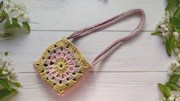 A small crochet granny square bag on white wooden boards.