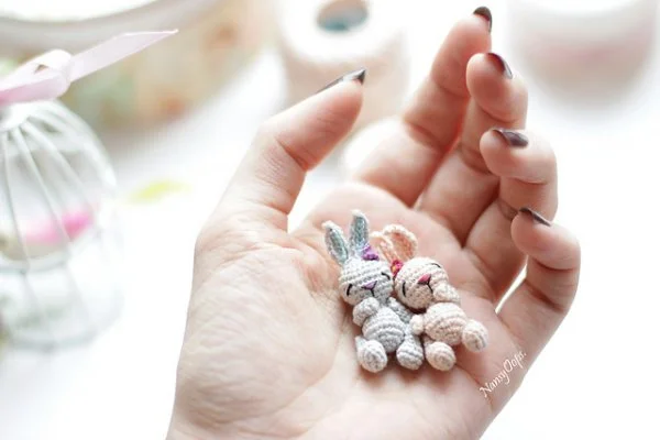 Two tiny crochet bunnies in the palm of a hand.