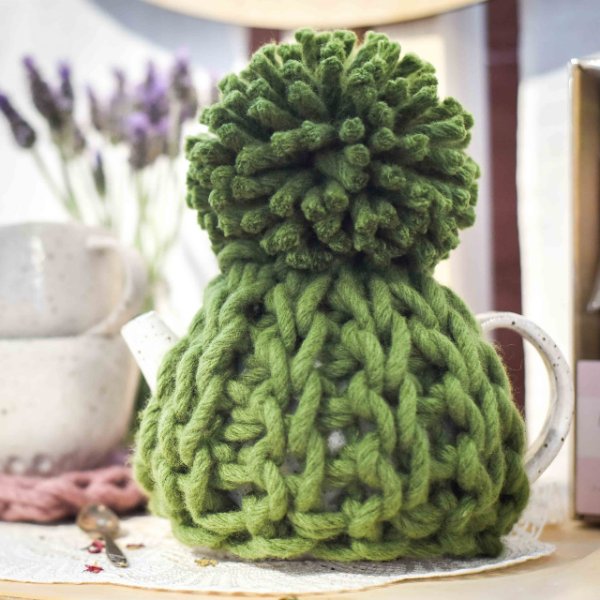 A green chunky crochet tea cozy on a stone teapot.