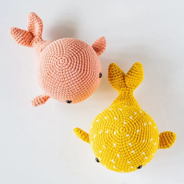 One pink and one yellow crochet whale toys.