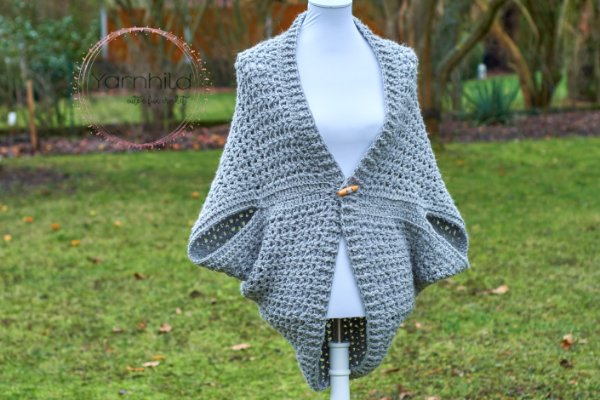 A mannequin with a grey crochet shrug with a wooden toggle closure.