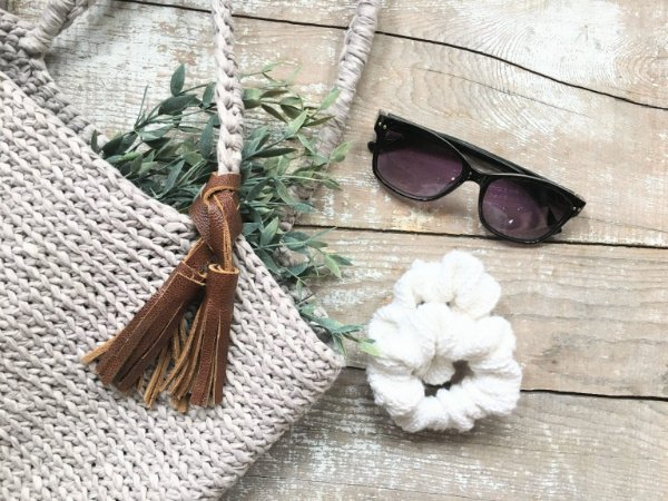 A white crochet scrunchie next to sunglasses and a bag