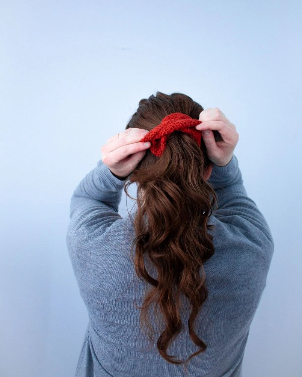 A woman putting her hair up in a red crochet scrunchie.