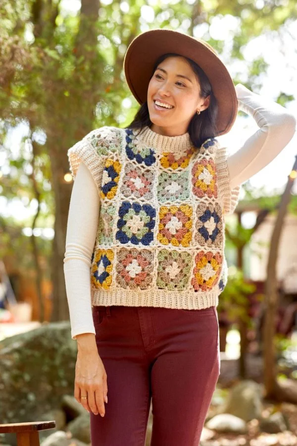 A woman in a hat, jeans, and a retro granny square crochet sweater vest.