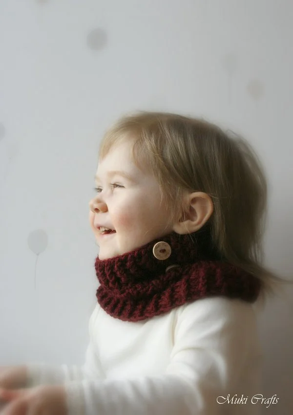 A profile view of a child with a burgundy crochet cowl.