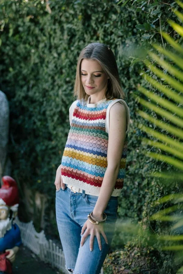 A woman in a garden with a rainbow-striped crochet sweater vest 