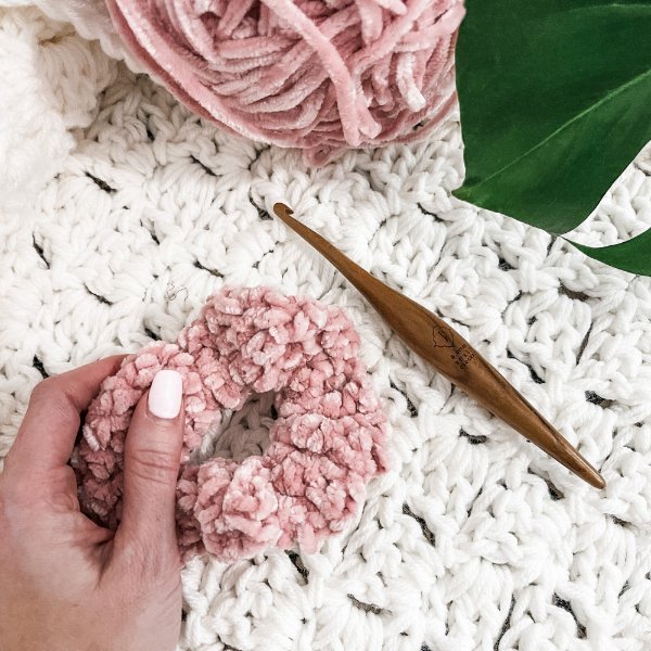 A pink velvet crochet scrunchie and a wooden crochet hook.